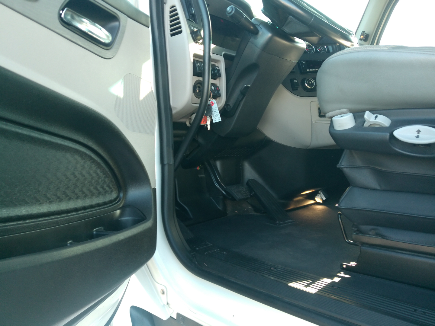 Interior of a Peterbilt 579 cab showing the driver seat and dashboard; open door and pedals visible.