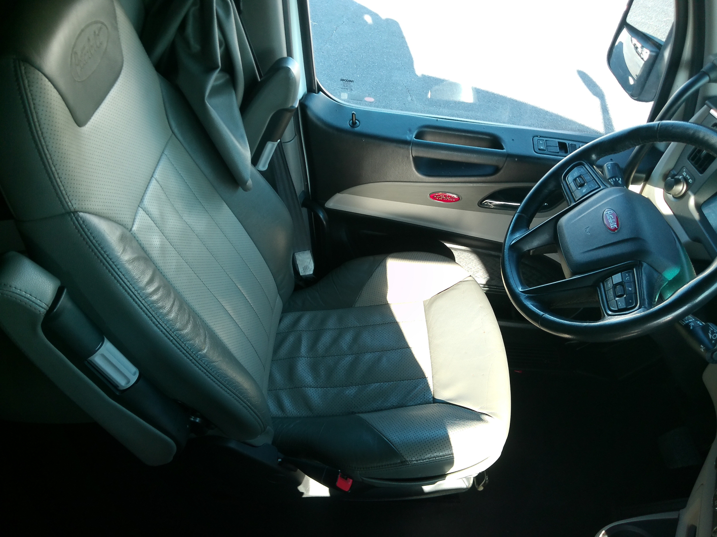 Peterbilt truck interior view showing driver seat, steering wheel, dashboard, and door panel. Text visible includes Peterbilt logo on seatback, and general cockpit layout.