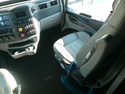 Truck cabin interior of a 2023 Peterbilt 579 with steering wheel, dashboard controls, and driver seat shown from the passenger side.