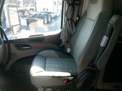 Peterbilt truck cab interior showing driver seat with light gray upholstery, window and door panel visible, curtain in the background.