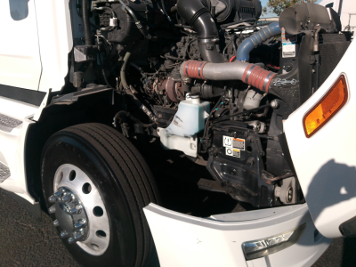 Peterbilt 579 engine bay showing intake hoses, coolant reservoir, radiator, and front wheel with hubcap.