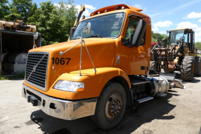 Volvo VNM42T conventional daycab truck with orange cab and black grille showing number 1067 on door.