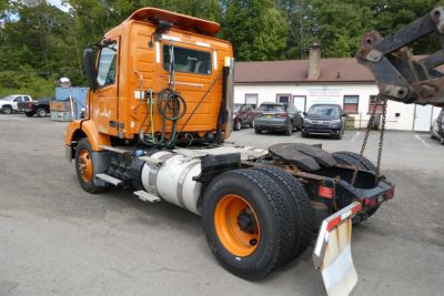 Volvo VNM42T daycab truck seen from rear-left side showing cab, fuel tank, and chassis with hook lift attachment.