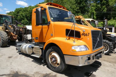 Volvo VNM42T conventional daycab truck in orange front-left view showing side fuel tank and wheel with number 1067.