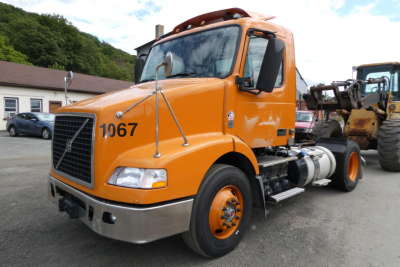 Orange 2014 Volvo VNM42T daycab truck front-right view showing number 1067 and stock area