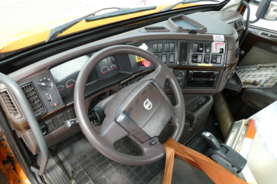 Truck cab interior showing steering wheel with Volvo logo, dashboard gauges, multiple control panels, and center console. Visible text includes no-gear labels or numbers; no clear model badges readable in this image.