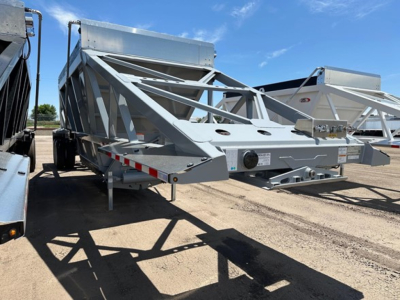 Trailer showing light-weight bottom-dump frame with truss supports and storage box, metal silver finish, landing gear, and wheel assemblies visible.