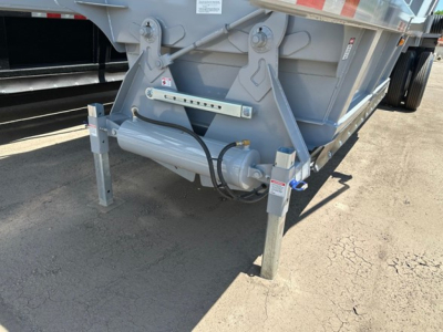 Bottom dump trailer showing hydraulic actuator and support legs with safety pins and structural frame, rear end mounted on legs.