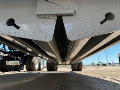 Underbelly view of a new CPS light weight bottom dump trailer showing dissected frame and axle area with yellow dirt, from ground level