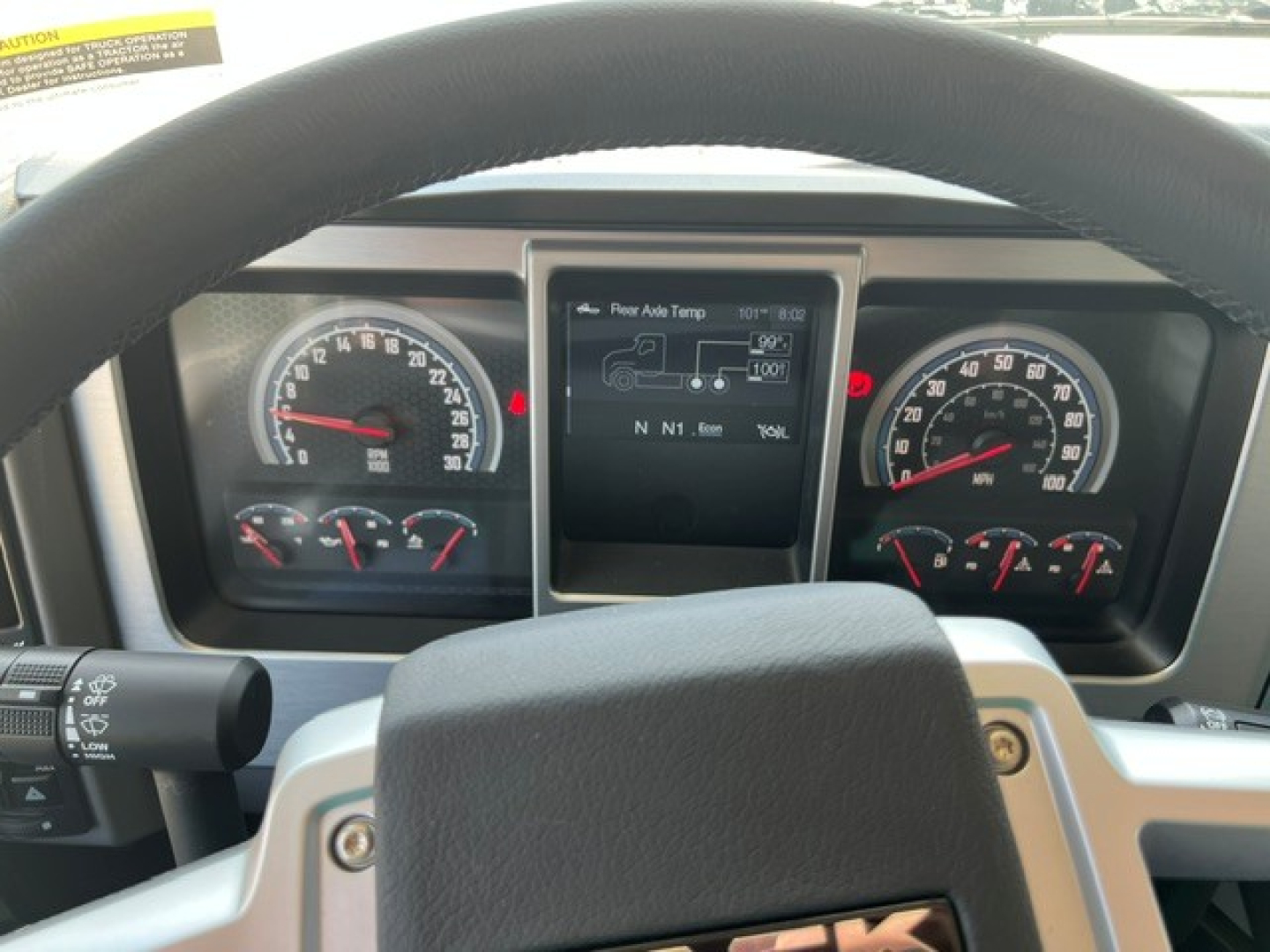 Truck cockpit of a 2027 Mack GR104F showing steering wheel, instrument cluster with gauges, and center touchscreen display.