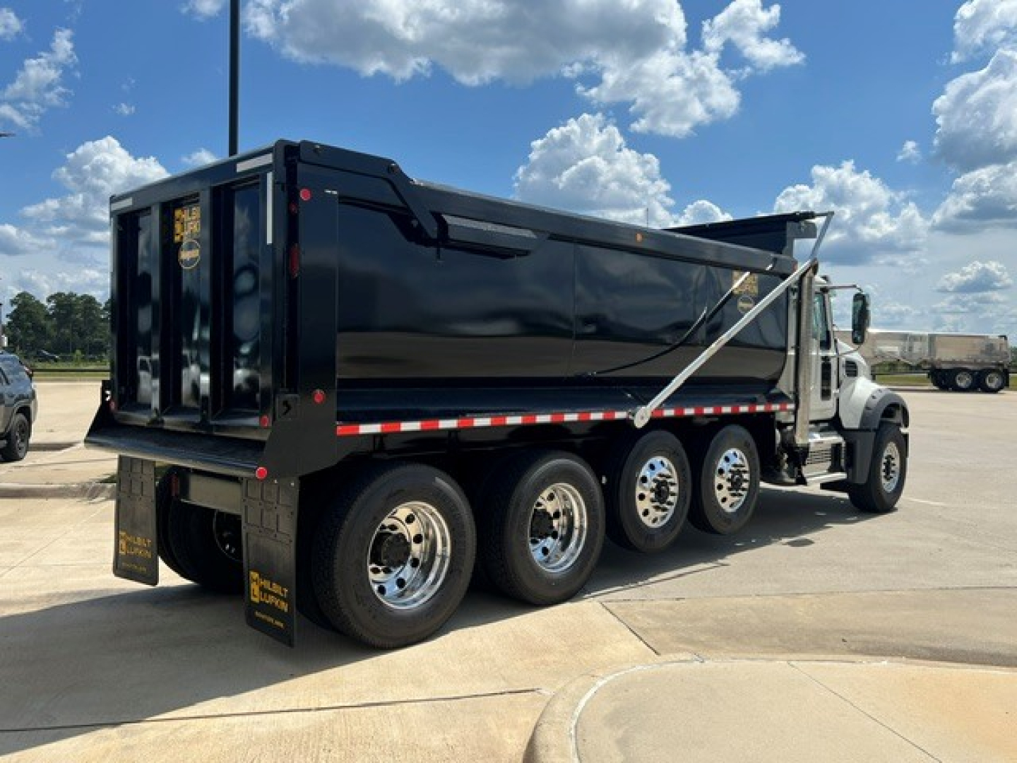 Dump truck showing side view of a black Mack GR104F dump body with six wheels, chrome rims, white cab, and red/white reflective striping along the lower body.