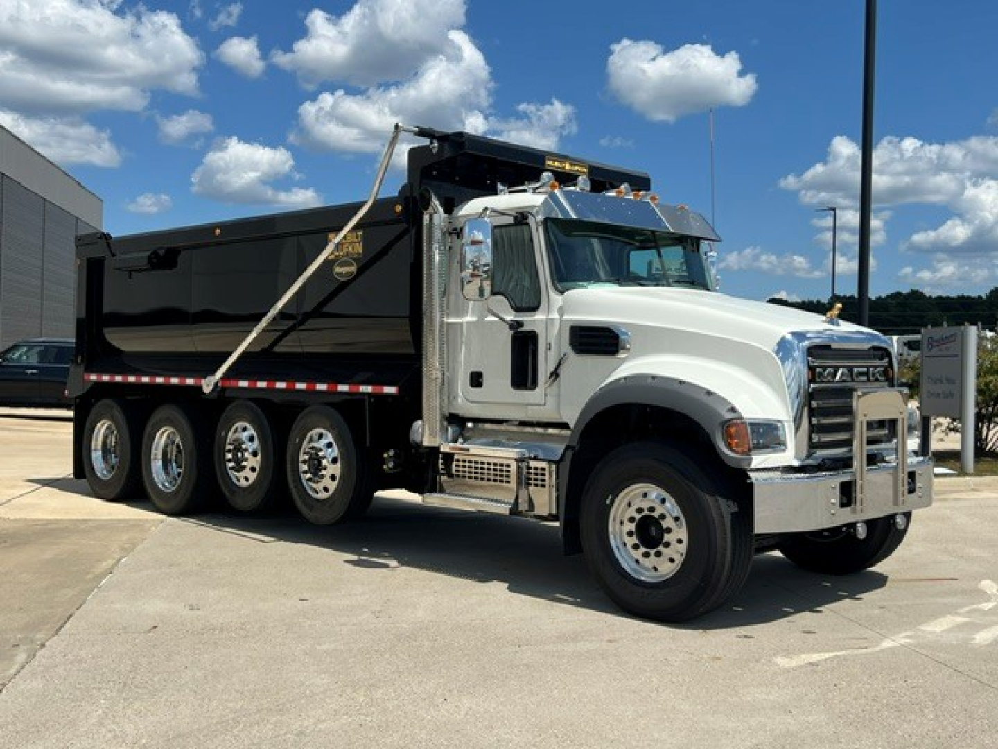 Dump truck 2027 Mack GR104F with white cab and black dump body, side view showing multiple rear axles and chrome grille.