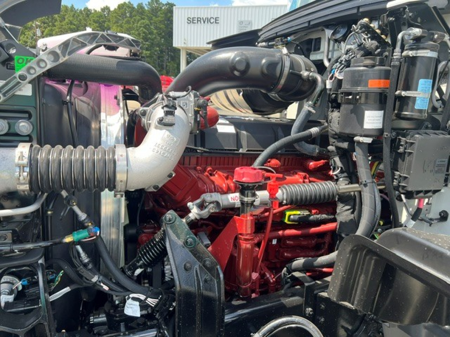 Engine bay of a 2027 Mack GR104F dump truck showing red diesel engine block, intake manifold, hoses, and various fluid reservoirs.
