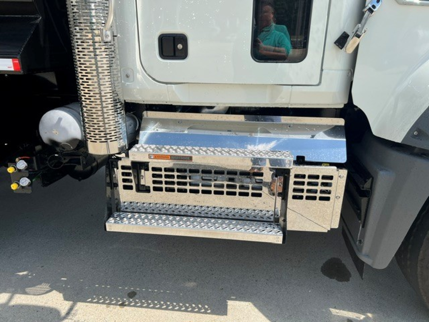 Truck side view showing chrome diamond-plate step and grille area beneath cab of a Mack GR104F dump truck.
