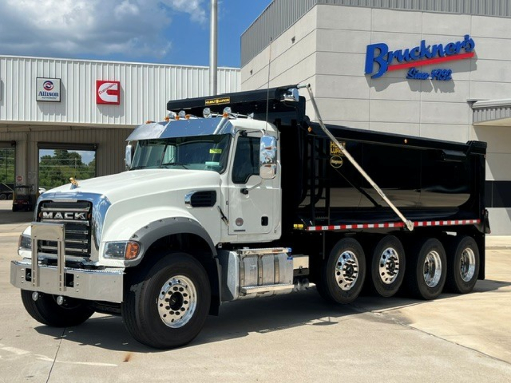 Dump truck showing Mack GR104F in white cab and black dump body with triple rear axles at dealership.