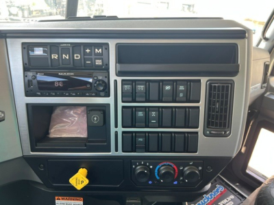 Dashboard of a 2027 Mack GR104F dump truck showing gear selector panel, climate controls, and various switches with a yellow removable key in the lower-left; vents and digital readouts visible.