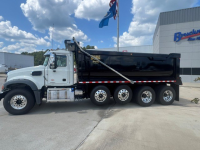 Dump truck side view showing large black dump body and white cab with chrome accents and six wheels on the rear; Mack GR104F style chassis