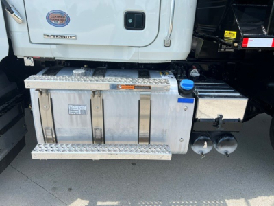 Aluminum side toolbox and fuel tanks under the cab of a white Mack GR104F dump truck showing metal steps and storage compartments.