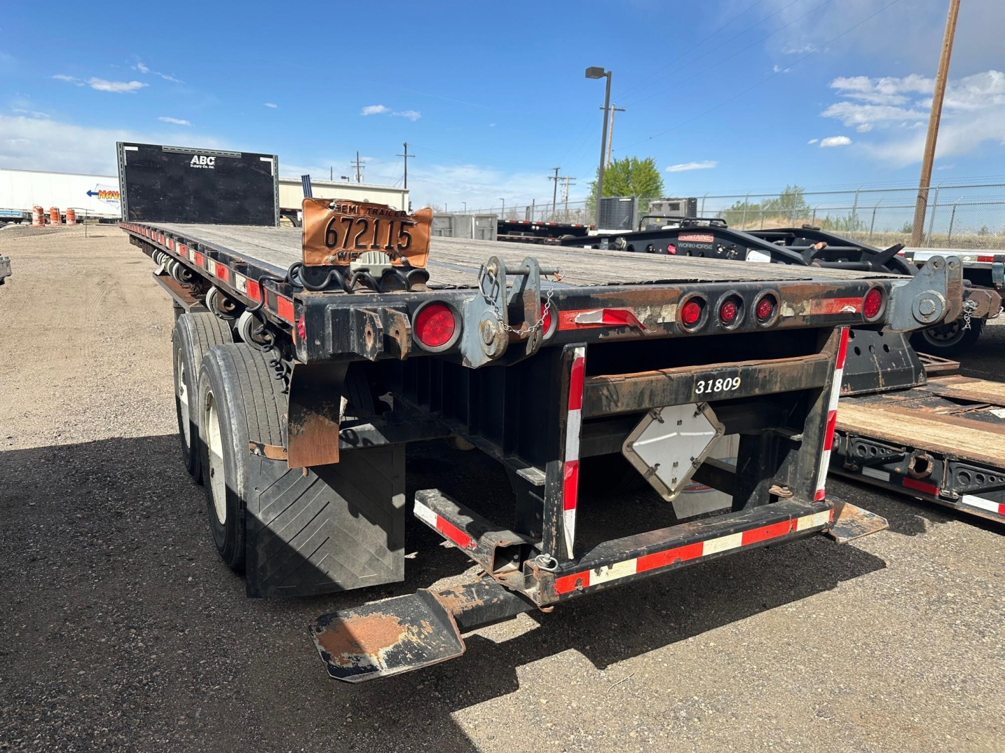 Trailer rear view of a 2015 Clark flatbed trailer with black frame, wood deck, multiple red tail lights, and a towing hitch plate.