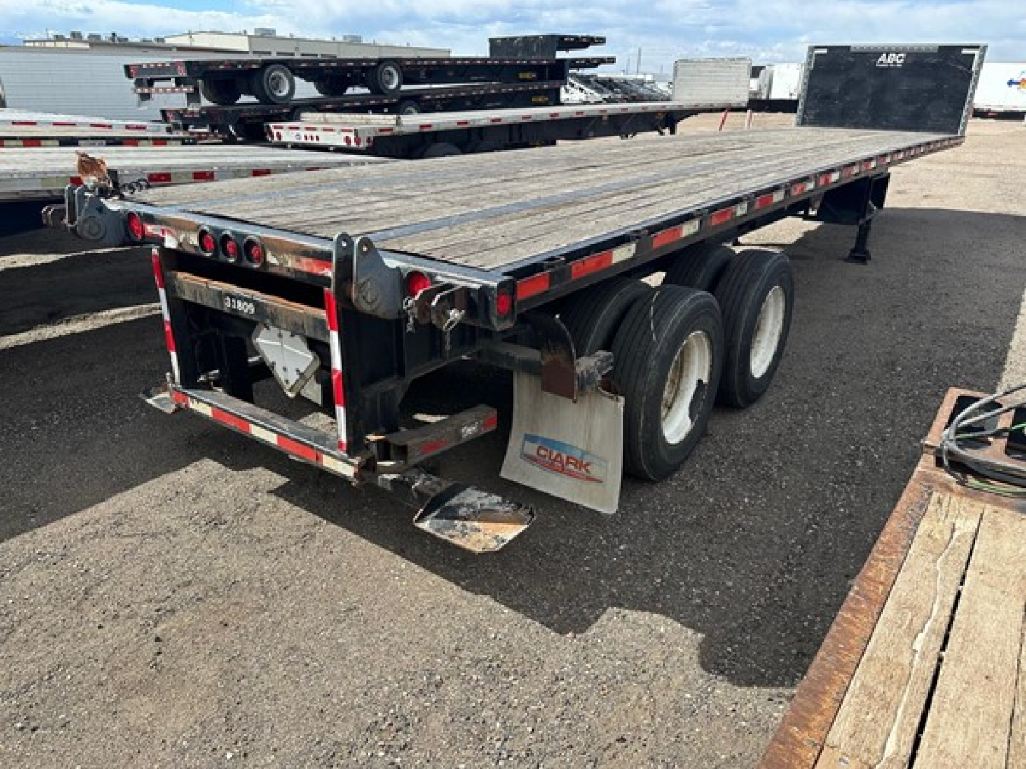 Flatbed trailer showing 38' steel deck with triple axle and forklift kit donor. Rear tail lights and mud flaps, Clark branding, and wood deck surface.