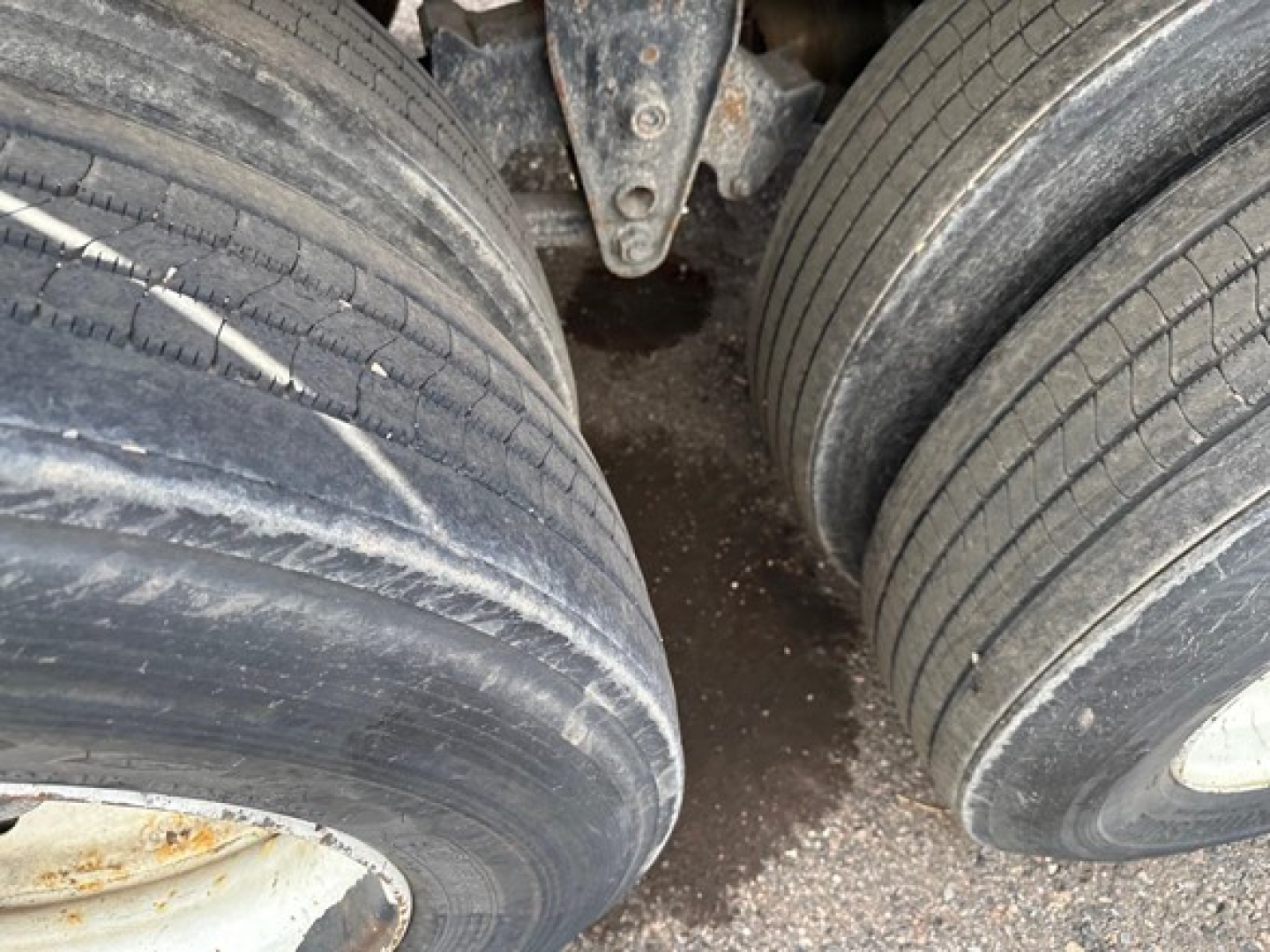 Trailer wheels and dual-tire axle showing worn tires and dry ground beneath.