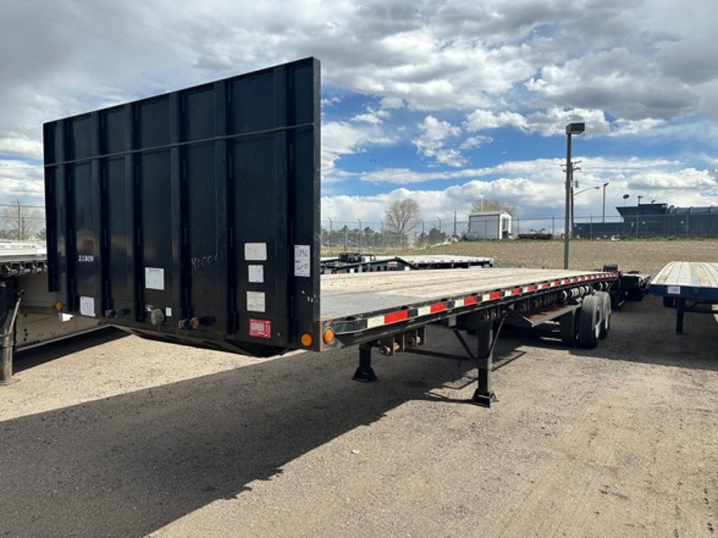Flatbed trailer with wood deck kit and forklift support, 38 feet, steel construction, rear ramp/tilt gate, parked in lot.