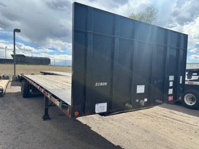 Flatbed trailer with forklift kit and wood deck showing rear end and side parking leg, ID numbers and stickers visible on back panel.