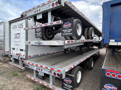 Flatbed trailer on a dual-deck trailer showing spare wheels and safety striping with Legend branding and Utility sticker visible