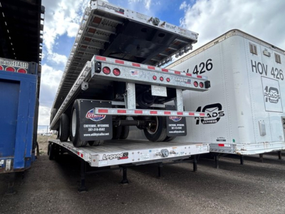 Flatbed trailer with folded flatbed on a Legend trailer undercarriage showing rear lights and rear bumper; number 426 on side of nearby trailer.