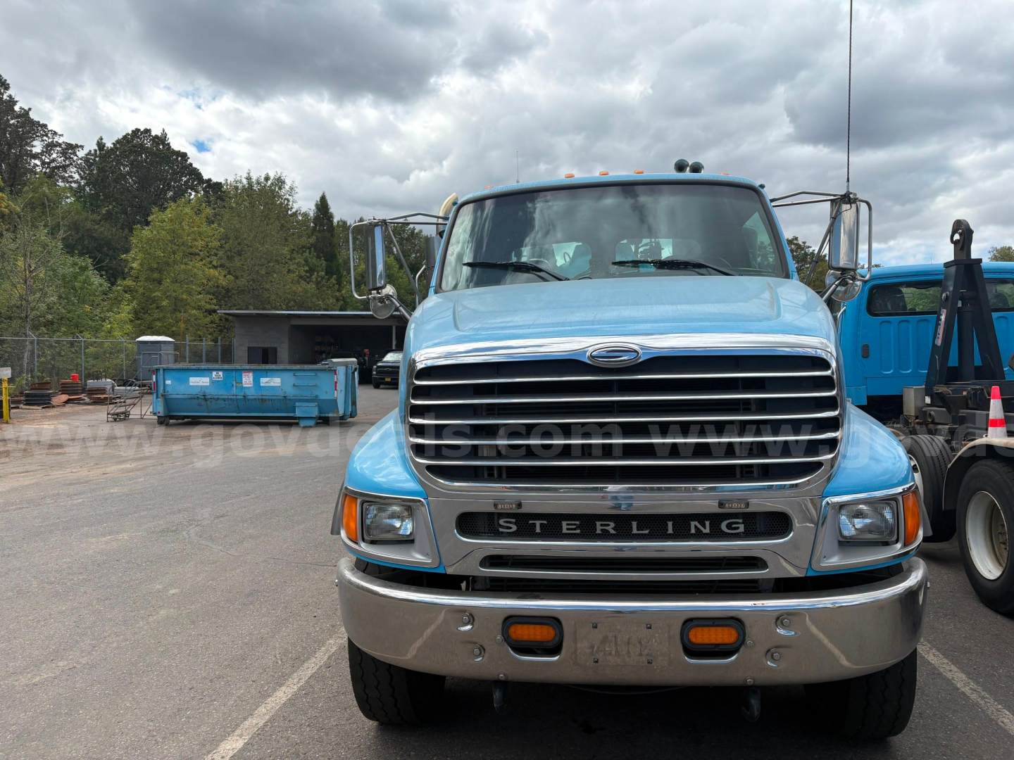 Front view of a blue Sterling LT9500 truck showing chrome grille with 'STERLING' and bumper; headlights; license plate area; side mirrors; blue sky with clouds.