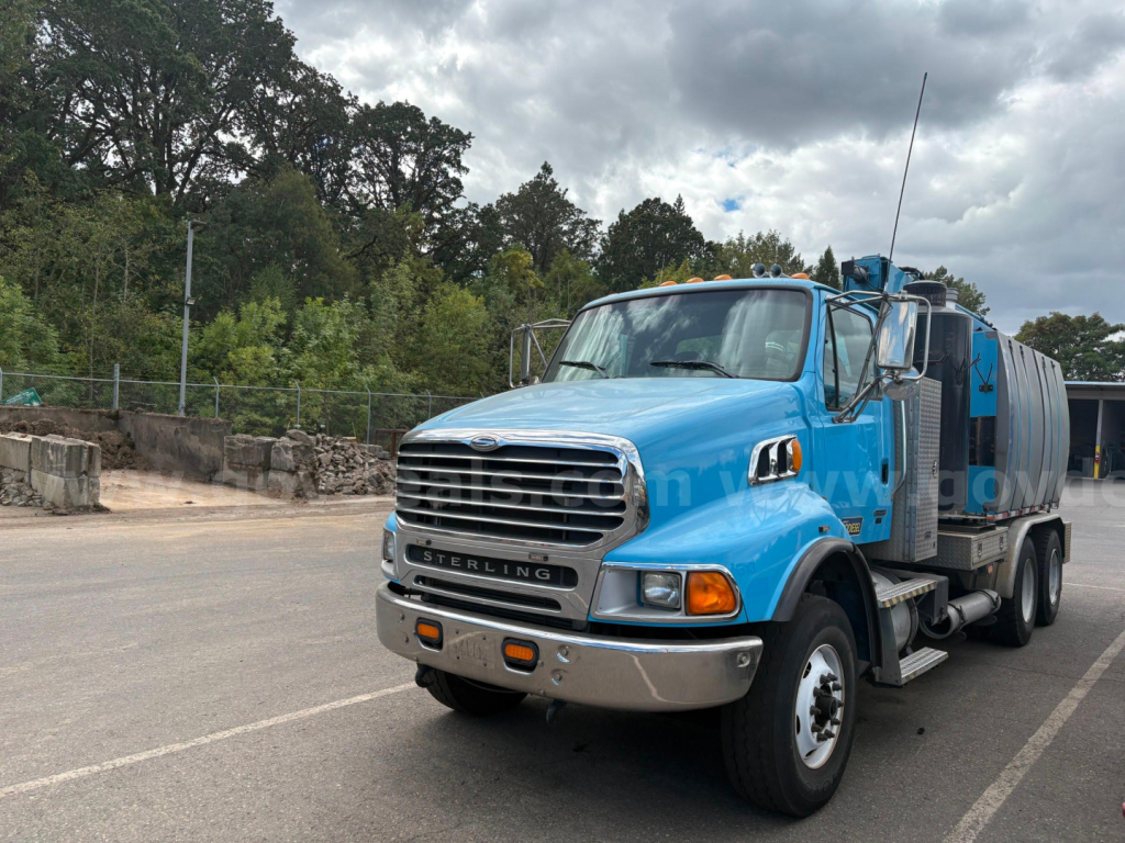 Sterling LT9500 vacuum truck front-left view with blue cab and metal tank, showing front grille, headlights, chrome bumper; no visible text besides 'STERLING' on grille.
