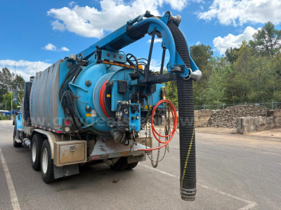 Vacuum truck rear view with large blue tank, hoses, and reel; circled area shows hoses and connector fittings.
