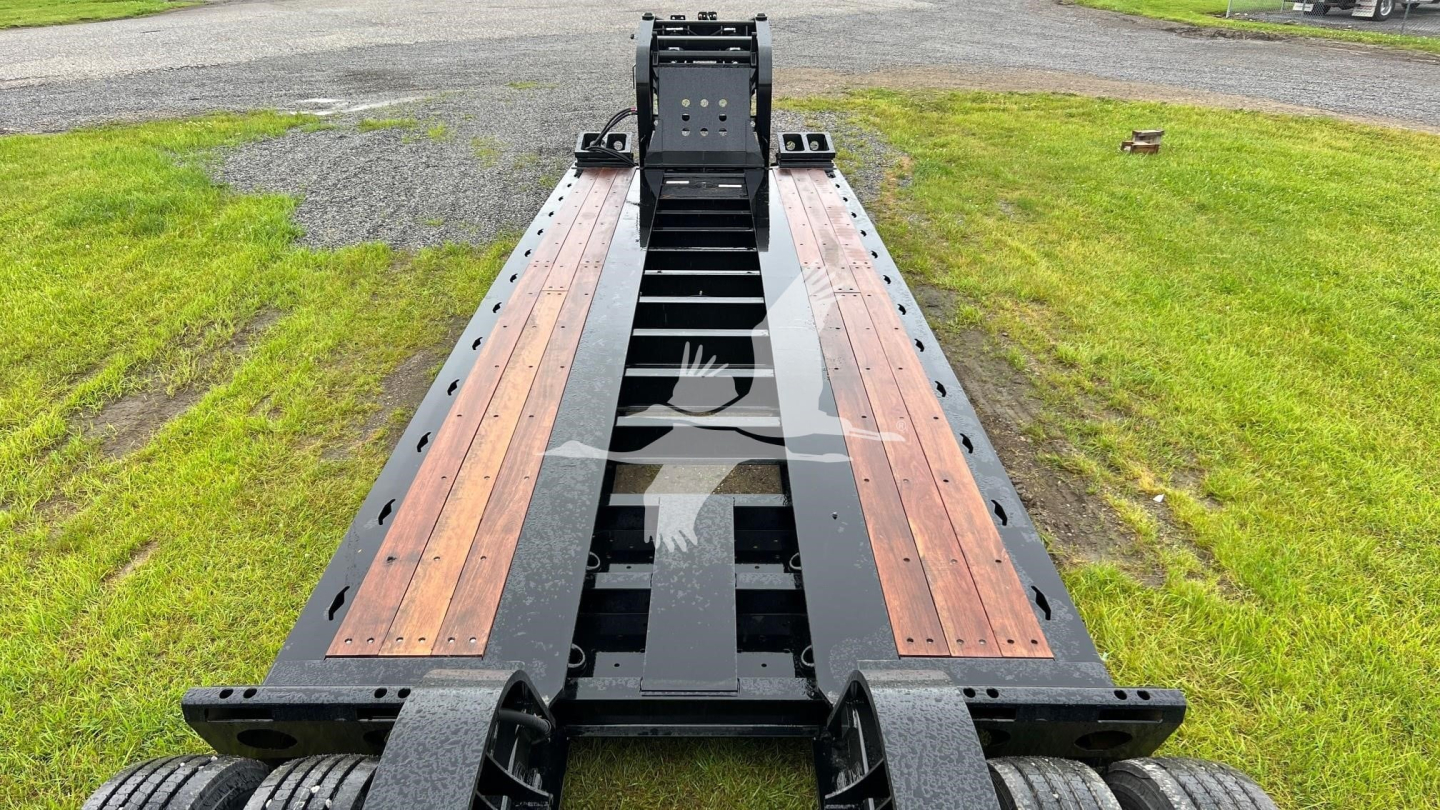 Lowboy trailer deck showing tandem frame rails with wooden deck inserts and black steel chassis for Fontaine 55 Lcc, in-service condition