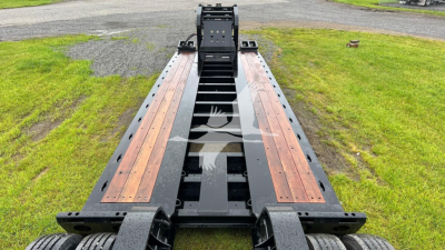Lowboy trailer deck showing tandem frame rails with wooden deck inserts and black steel chassis for Fontaine 55 Lcc, in-service condition