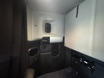 Truck cab interior view of a 2023 Kenworth T680 sleeper, with light gray seats and black panels; no visible text on components.