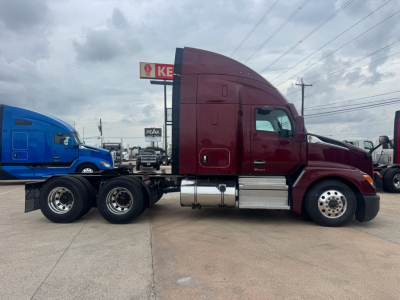 Kenworth T680 conventional sleeper truck in maroon with blue tractor on a trailer, side view showing cab, fuel tanks, and wheels.