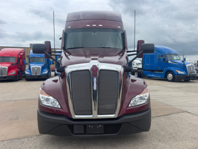 Kenworth T680 front view showing large chrome grille, maroon body, black bumper, and trapezoid headlights in a truck lot.