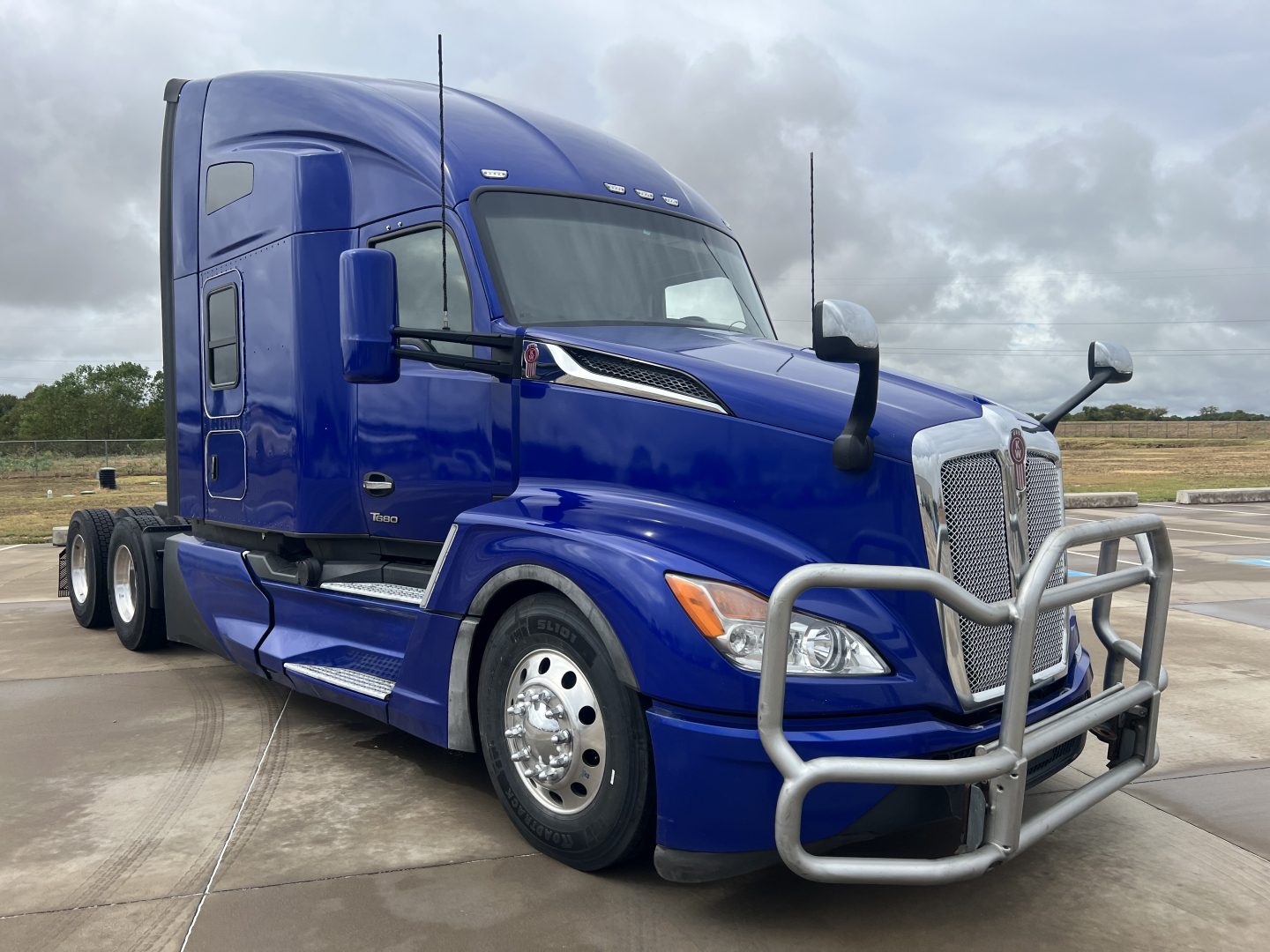 Kenworth T680 sleeper cab truck in blue, front-right view with grille guard and chrome wheels.