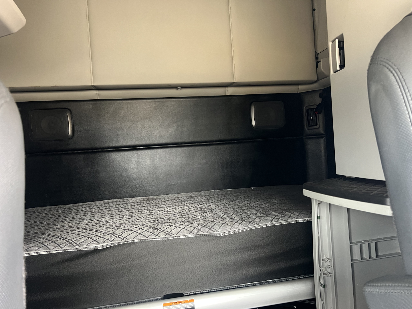 Kenworth T680 cab interior storage area with bunk bed behind the driver's seat; quilted mattress surface.