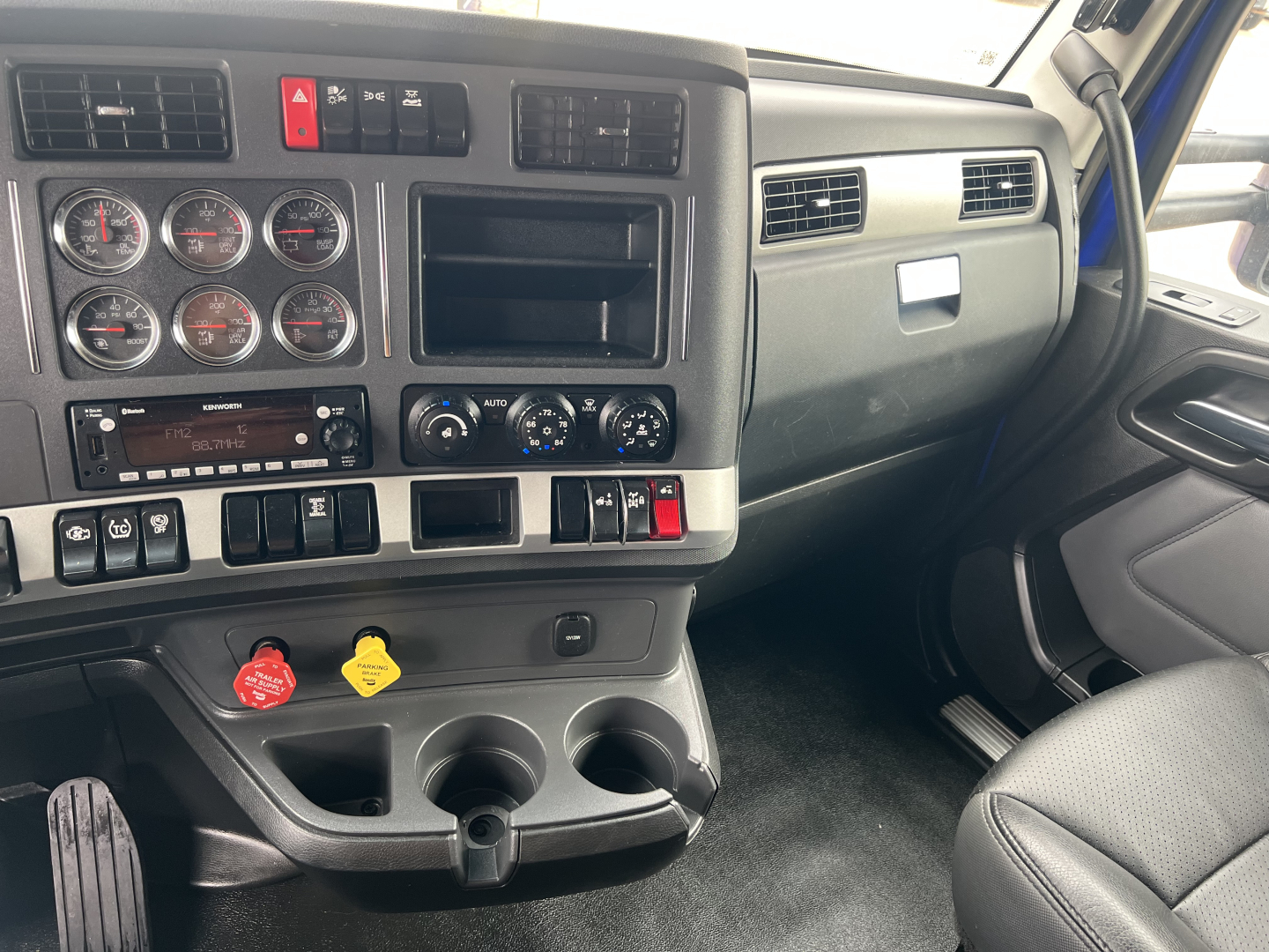 Kenworth T680 dash and driver-side interior showing gauges, controls, and cup holders in a conventional sleeper truck cab.