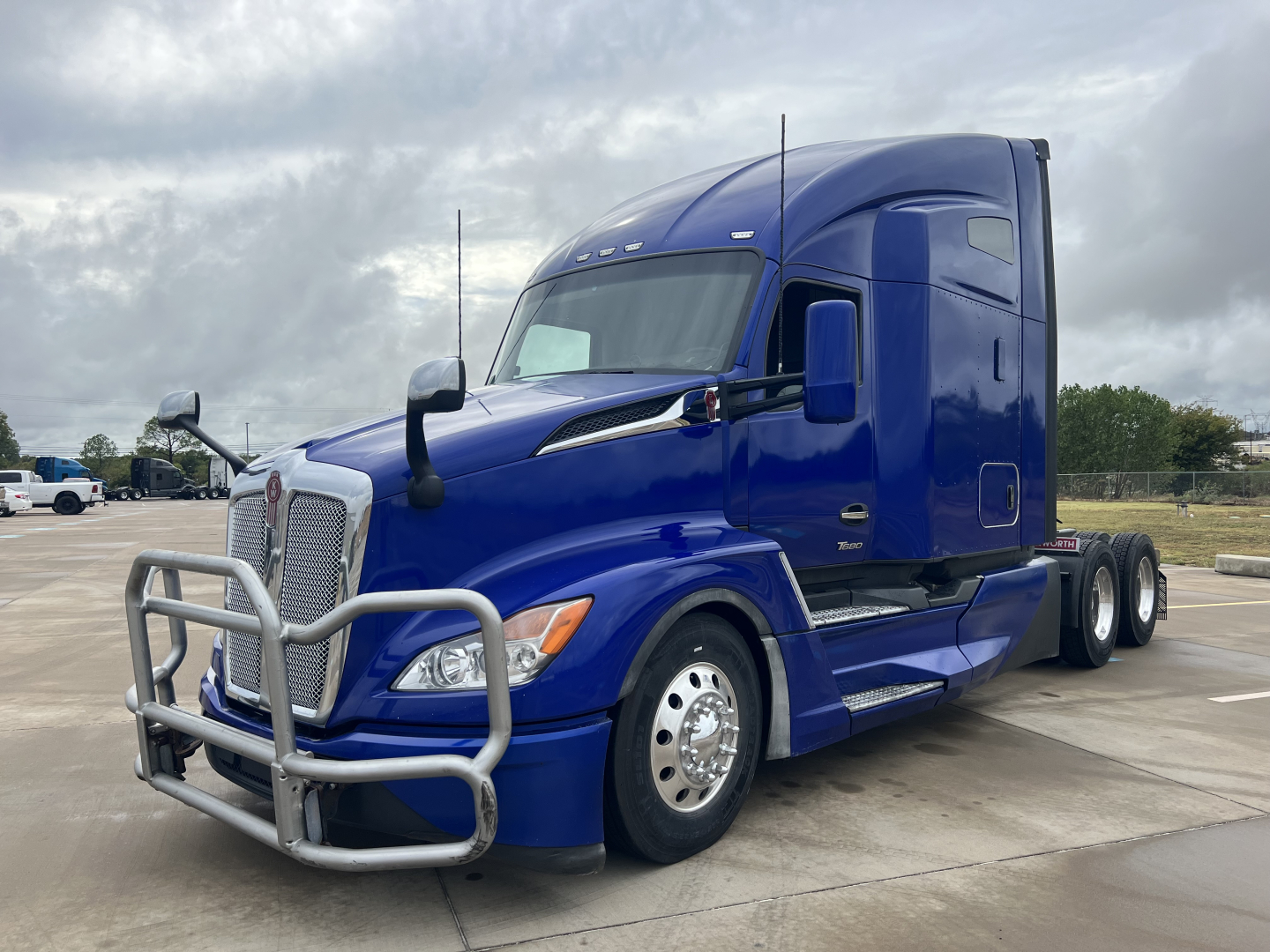 Kenworth T680 conventional sleeper truck in blue, front grille guard, side view showing dual rear axles and chrome wheels.
