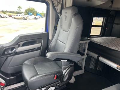 Kenworth T680 cab interior showing driver seat and sleeper area with side door panel and bed in background.