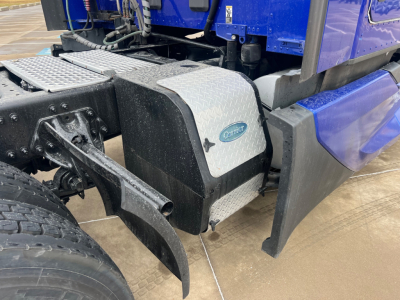 Kenworth T680 truck chassis side showing fuel tank with diamond plate cover and blue cab. Parts visible include steps, frame, and rear wheel.