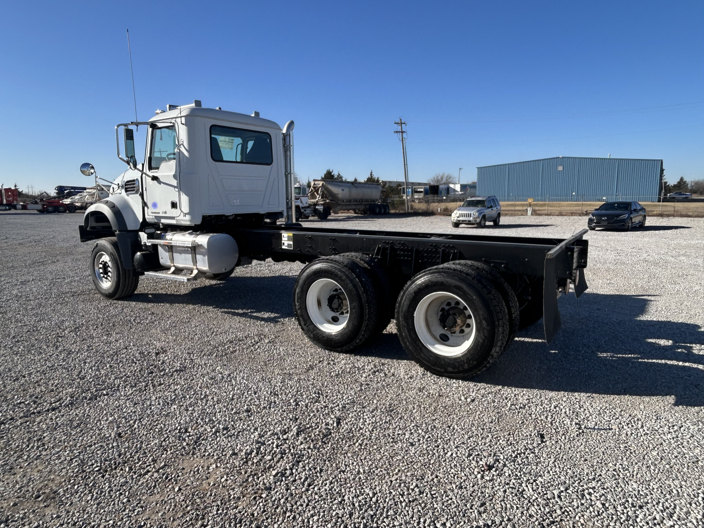 Mack GR64F cab chassis truck in a gravel lot, side view showing chassis and dual rear axles, cab with mirrors and steps, no bodybed installed.