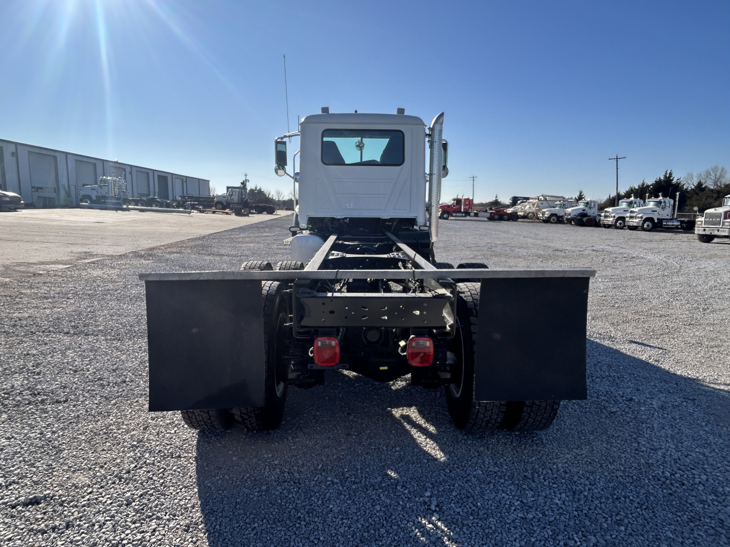 Rear view of a white Mack GR64F cab and chassis showing dual rear wheels, flatbed mudflaps, and chassis exposed.