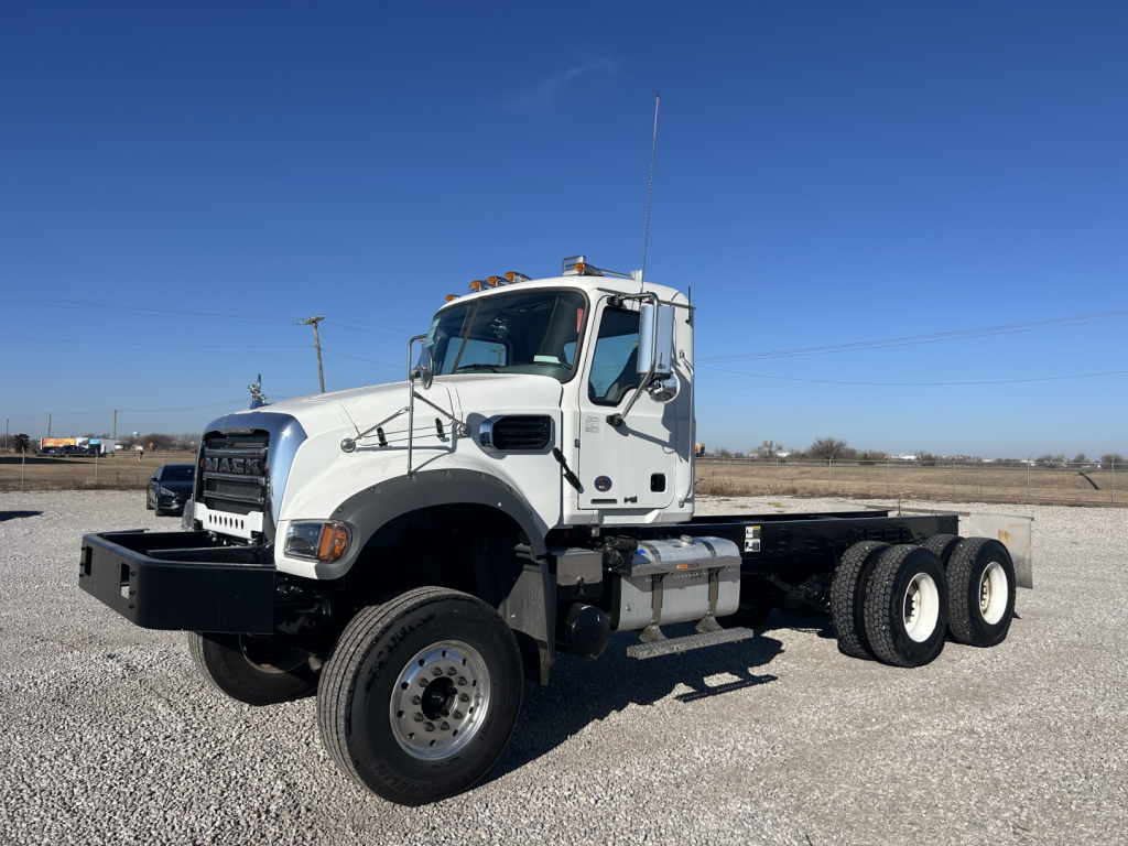 2026 Mack GR64F cab and chassis truck showing front left side with dual rear axles, white cab, black bumper, and long chassis