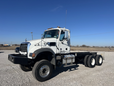 2026 Mack GR64F cab and chassis truck showing front left side with dual rear axles, white cab, black bumper, and long chassis