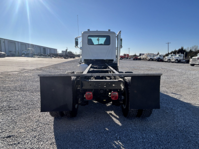 Rear view of a white Mack GR64F cab and chassis showing dual rear wheels, flatbed mudflaps, and chassis exposed.