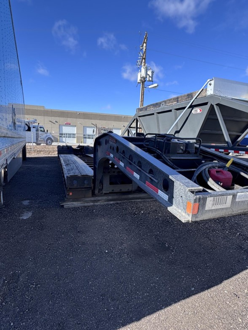 Lowboy trailer connection showing Fontaine 55 LCC trailer deck with gooseneck and hitch area, metal frame, and surrounding yard