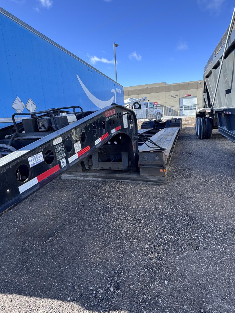 Lowboy trailer showing Fontaine 55 LCC with loading ramp and wheel area; visible text includes stock and vin labels and branding on equipment.